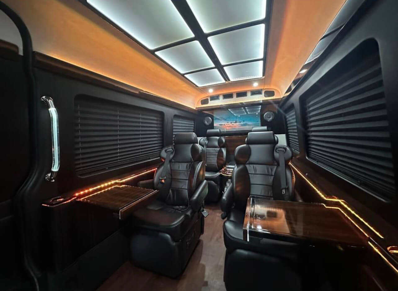 California Wine Tours luxury van interior with reclining black leather seats, wood tables, and ambient ceiling lighting