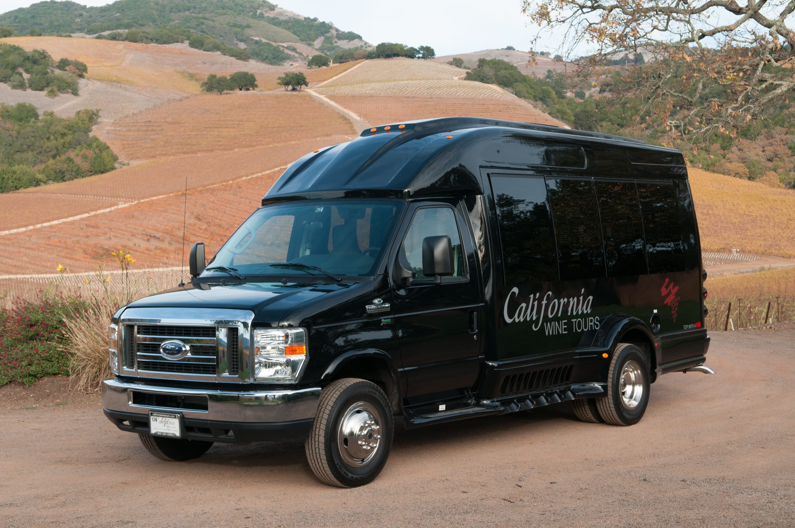 California Wine Tours shuttle bus parked beside vineyard hills, offering stylish group transportation for wine country trips.