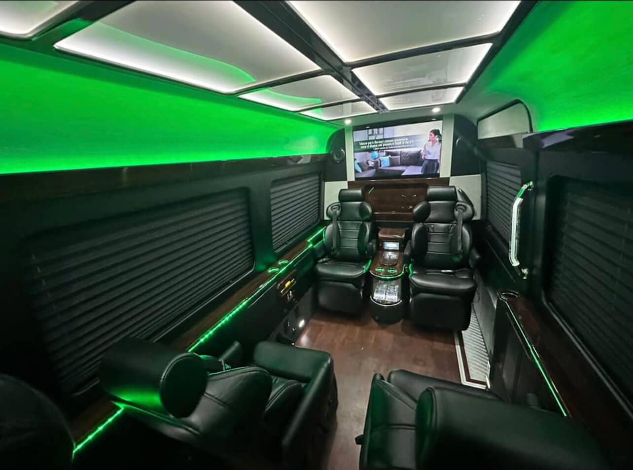Black leather recliners with green LED lighting and TV screen in a California Wine Tours luxury coach for premium travel.