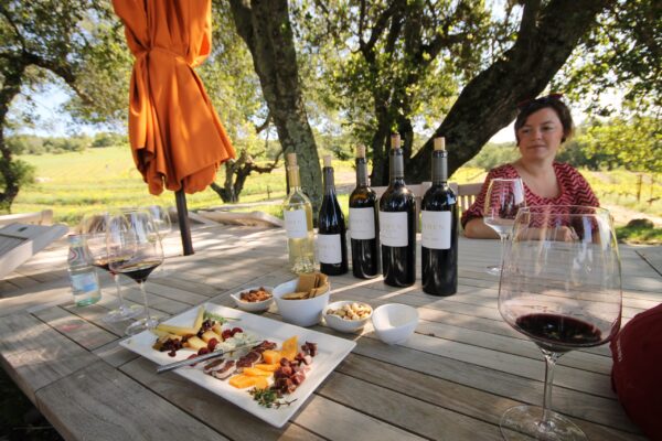 A woman at a table with food and wine bottles, engaged in a dining experience.