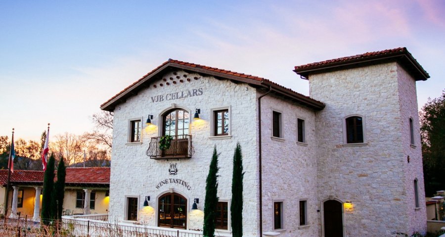 The VJB winery silhouetted against a vibrant sunset, with warm hues illuminating the vineyard landscape.
